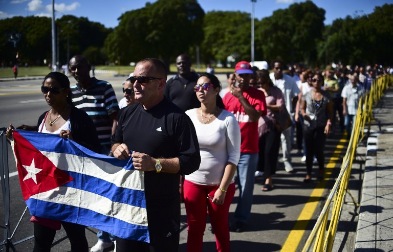 People holding a Cuban national flag queue to enter Jose Marti's memorial to pay their last respects to Cuban revolutionary icon Fidel Castro at Revolution Square in Havana, on November 28, 2016. A titan of the 20th century who beat the odds to endure into the 21st, Castro died late Friday after surviving 11 US administrations and hundreds of assassination attempts. No cause of death was given. Castro's ashes will go on a four-day island-wide procession starting Wednesday before being buried in the southeastern city of Santiago de Cuba on December 4. / AFP PHOTO / RONALDO SCHEMIDT
